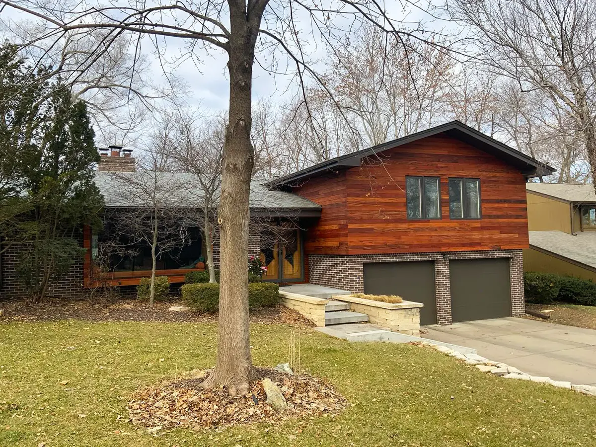 Suburban home featuring rich wood-toned siding and an updated exterior, blending with natural surroundings.