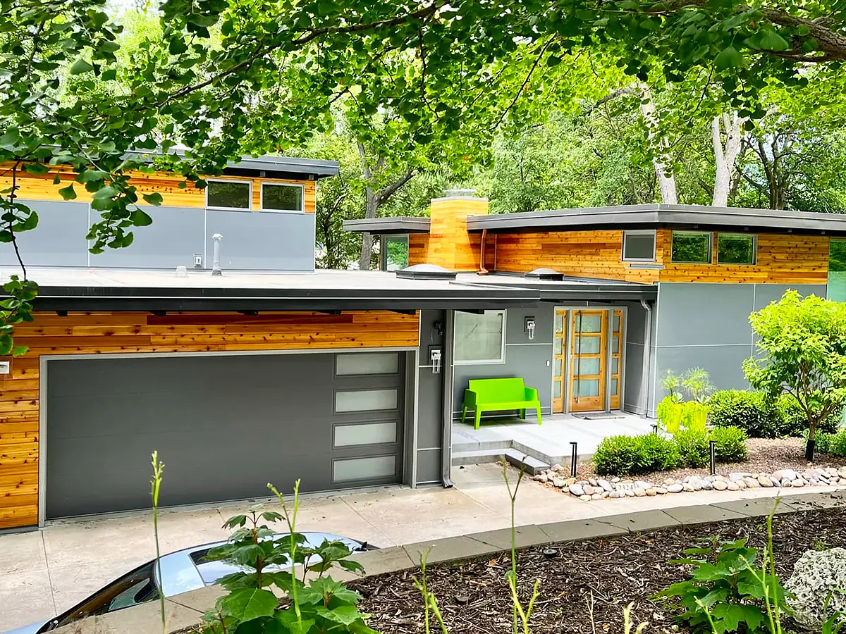 Modern home with sleek gray siding and wooden accents, surrounded by lush greenery after siding installation.