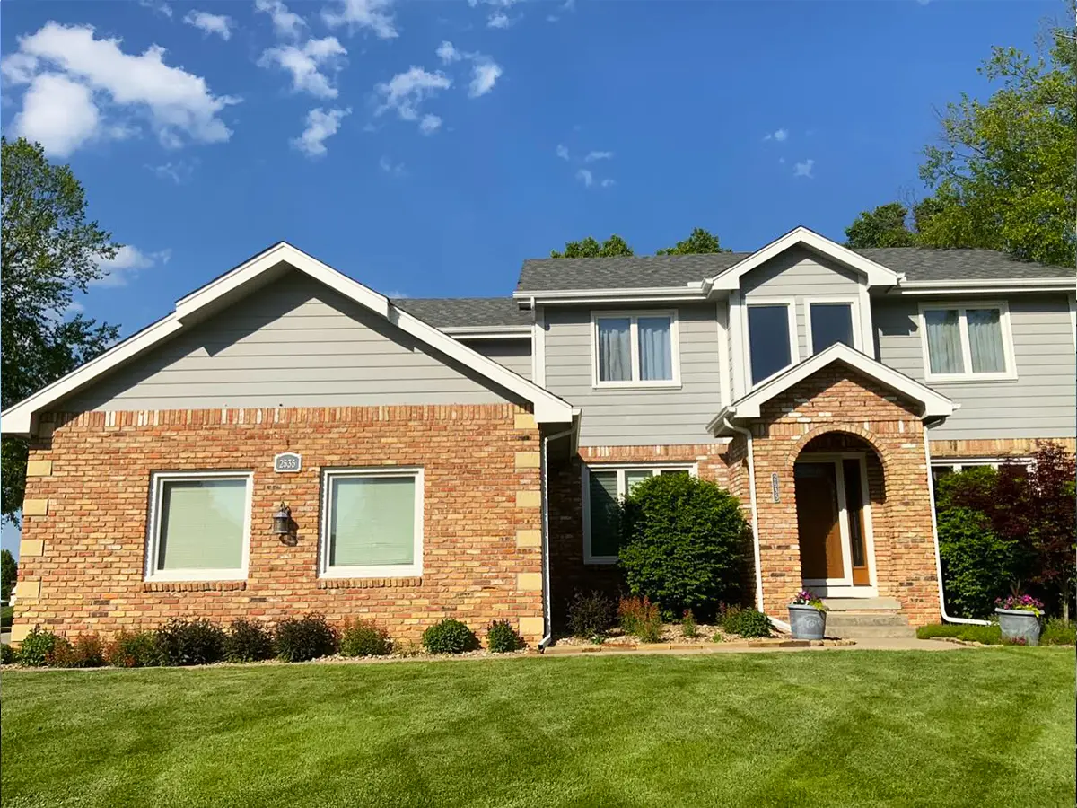 Brick and siding house with outdated exterior, set on a well-maintained lawn before siding renovation.