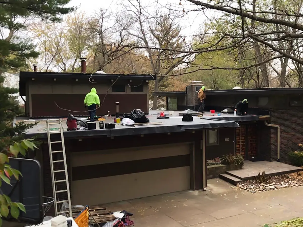 Workers preparing a home for siding installation, featuring a dark exterior and surrounding trees.