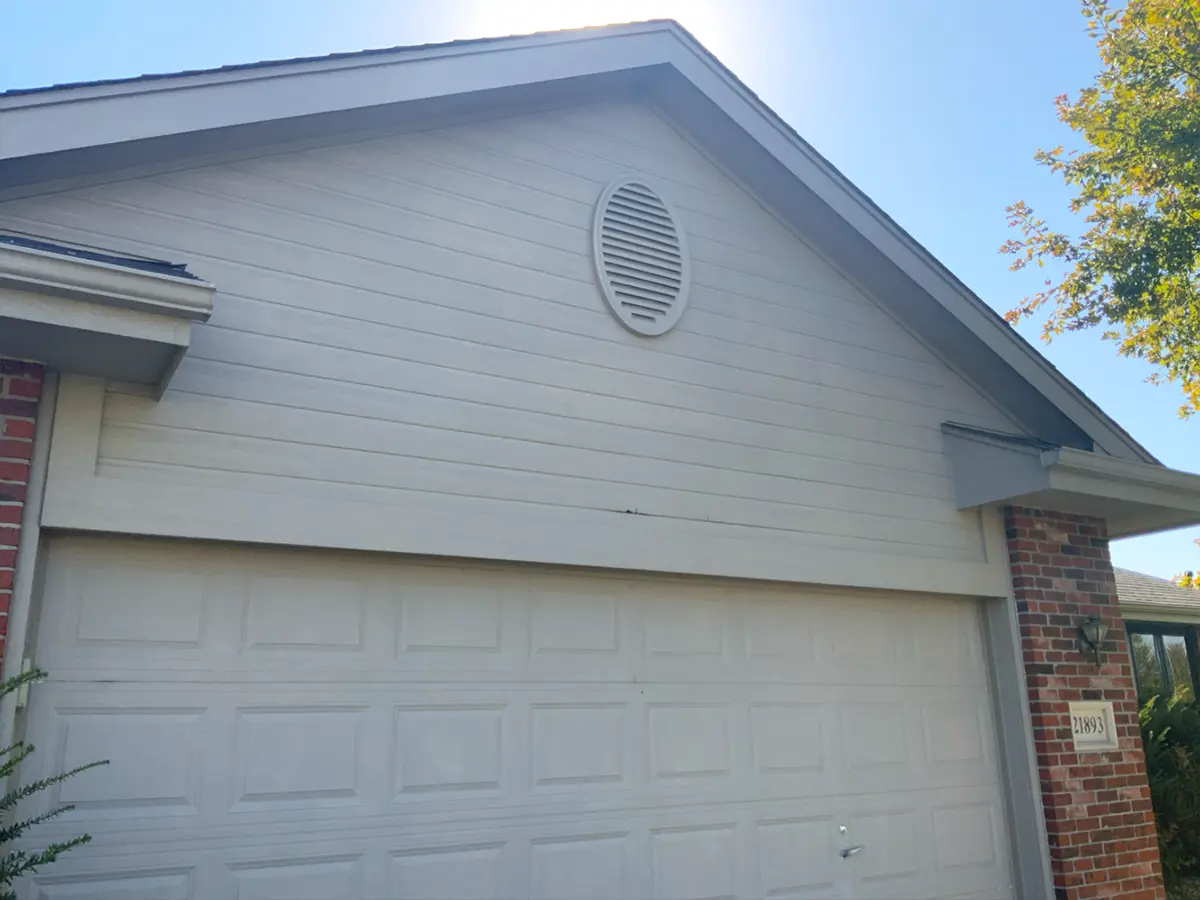 Garage and home exterior with worn siding showing cracks and discoloration before repair.