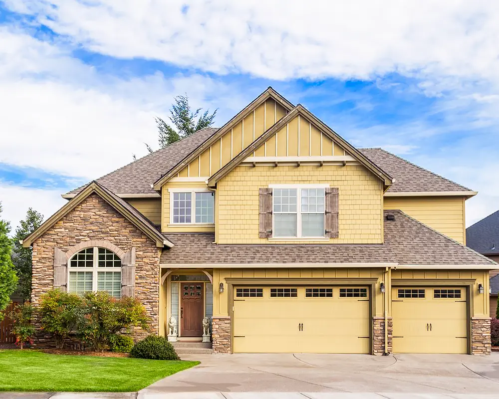 Two-story yellow house with a fresh shingle roof and stone accents, highlighting improved curb appeal and functionality.