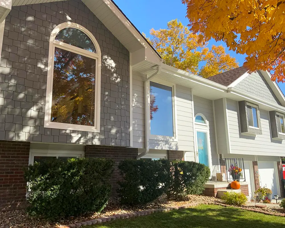 Suburban home with arched windows and updated siding, framed by vibrant autumn foliage and well-maintained landscaping.