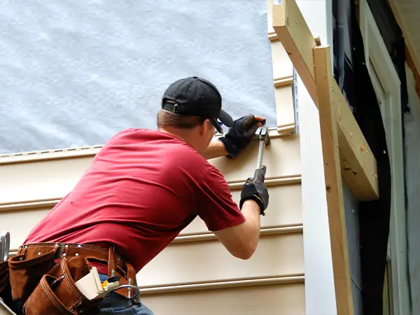 Worker installing siding panels on a home's exterior with precision and modern tools.