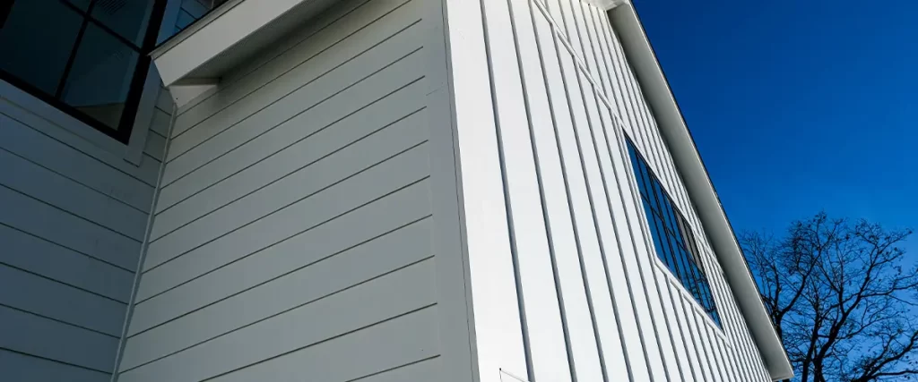 Bright white exterior featuring Fiber Cement Siding with black-framed windows, set against a clear blue sky.