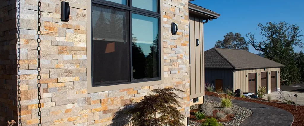 Stylish exterior featuring stacked stone veneer siding, black-framed windows, and a landscaped walkway.