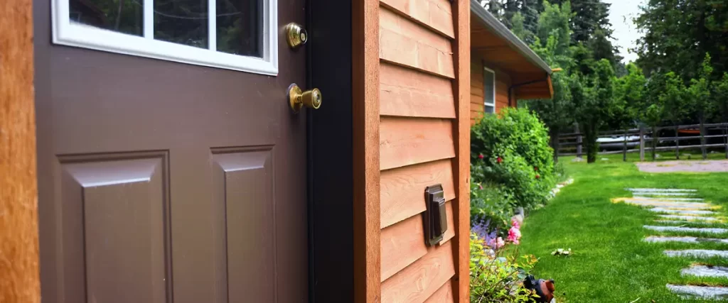 Warm-toned wooden siding with a brown front door, surrounded by lush landscaping and a stone pathway.